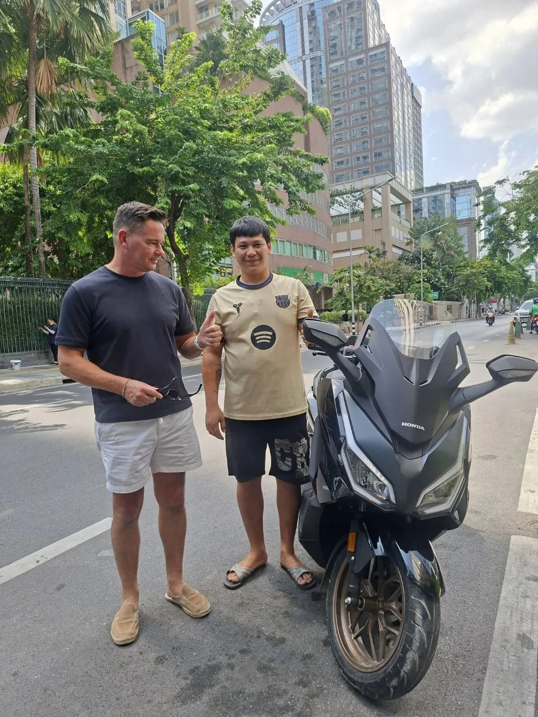 Two men with a Honda Forza at a kerbside handover on a central Bangkok street