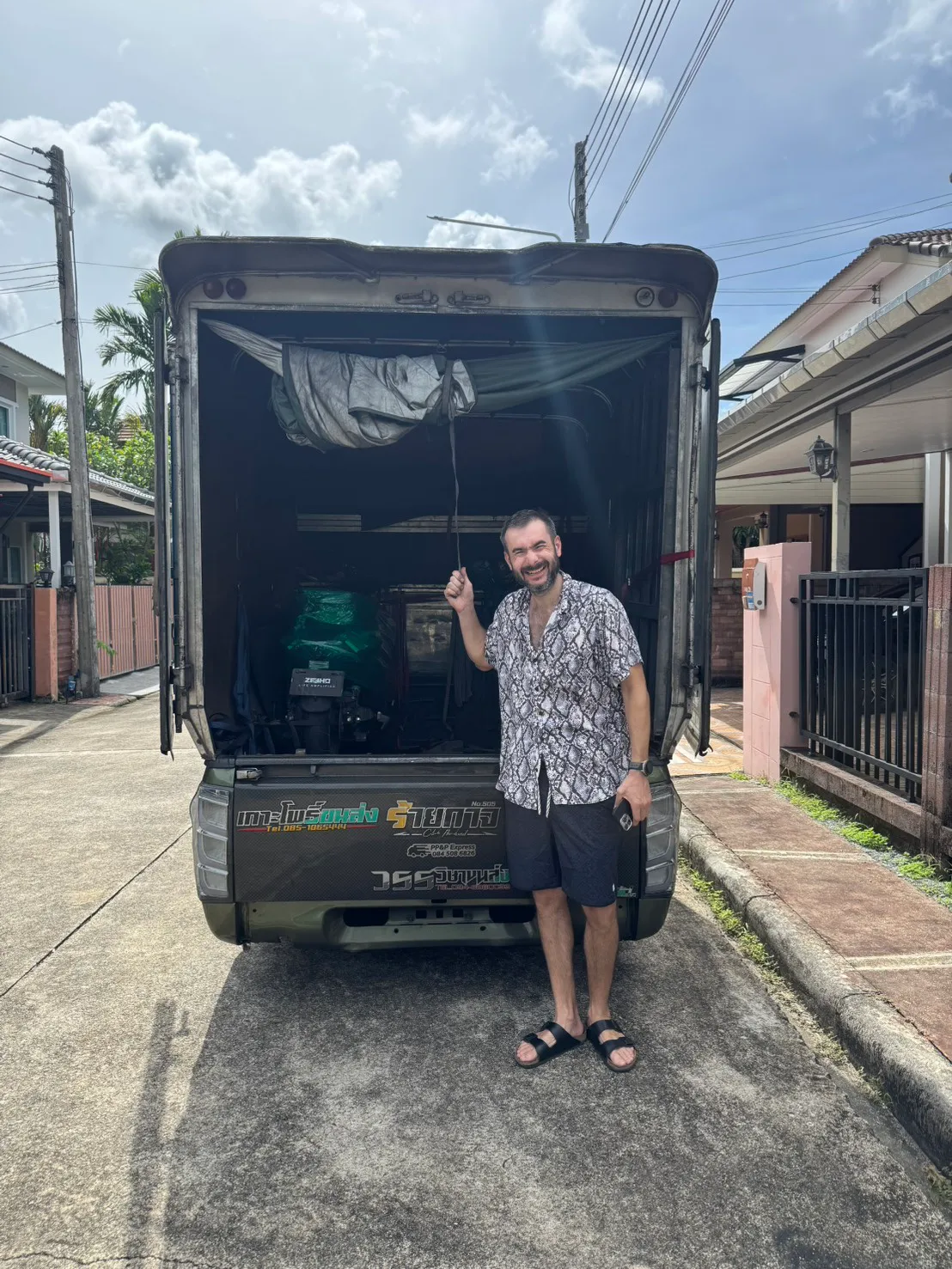 Smiling customer holding open the side curtain of a loaded transport truck outside a house